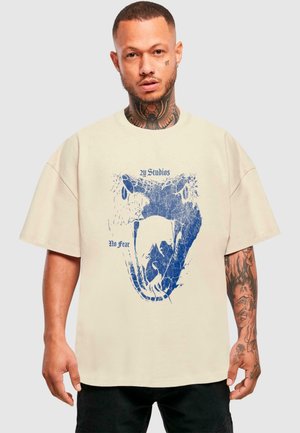 Beige oversized t-shirt med en blå grafik af et slangehoved og teksten "2y Studios" og "No Fear" på fronten.