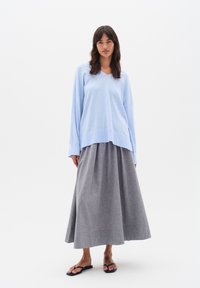 Světle modrý oversized svetr s výstřihem ve tvaru V, doplněný dlouhou šedou plisovanou sukní. Model má na sobě černé žabky. Jednoduché, jemné textury.