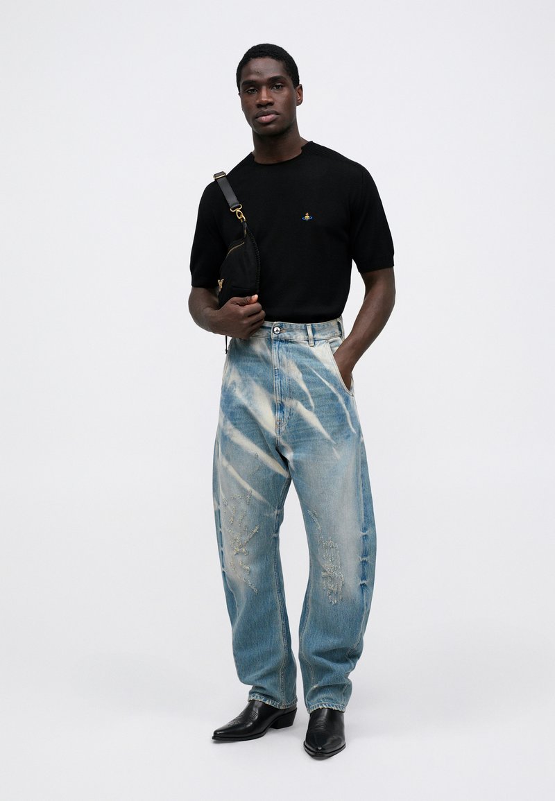 Svart kortärmad skjorta med logotyp, ljusblå slitna denimbyxor, hög midja, löst snitt, kombinerat med svarta spetsiga stövlar.