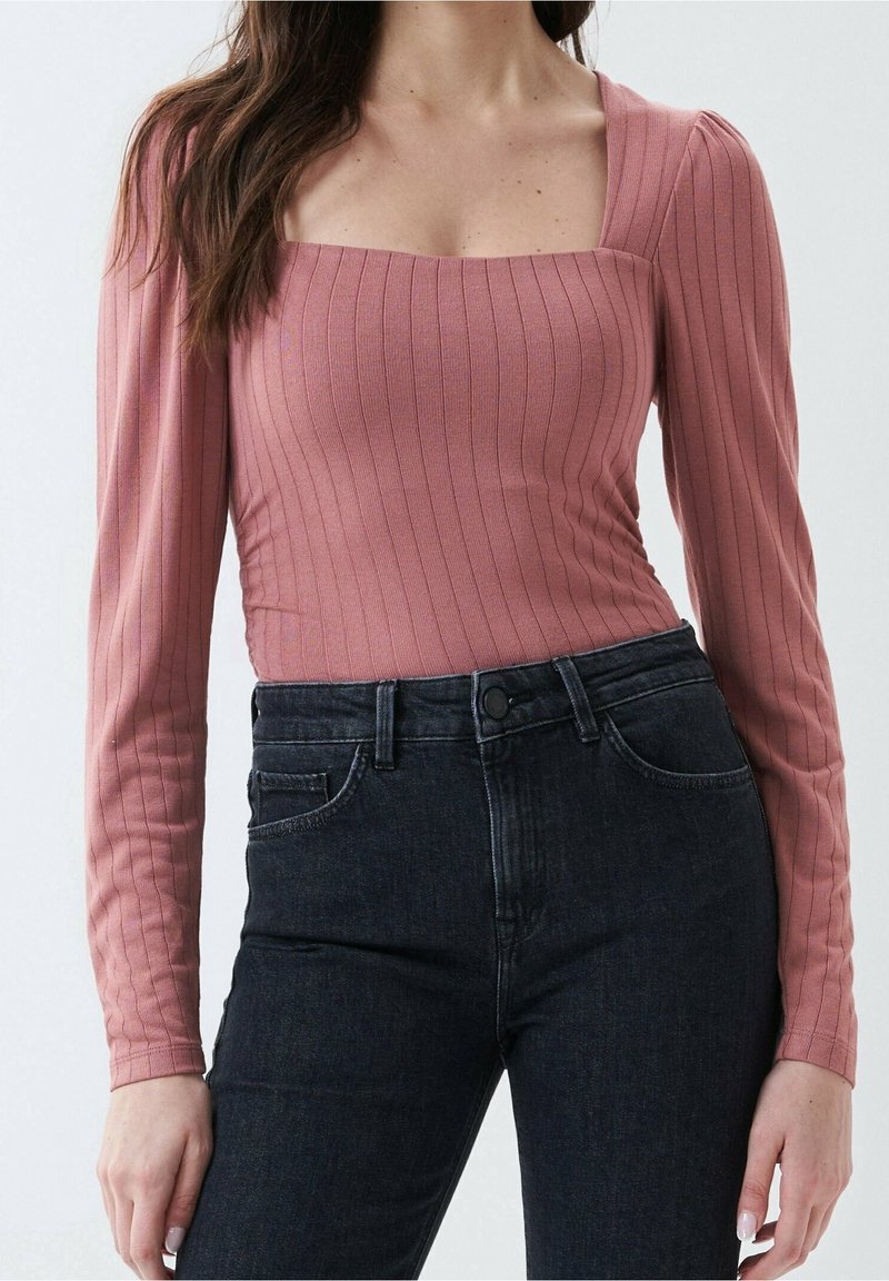 Långärmad, dammig rosa ribbad topp med fyrkantig halsringning, i kombination med högmidjade mörk denimjeans med en klassisk knapp och fickdesign.