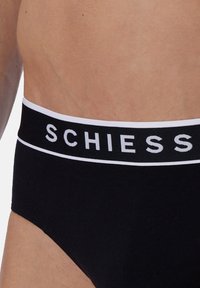 Slip nero con una texture morbida e un ampio elastico in vita con il nome del marchio "SCHIESS" in lettere bianche su uno sfondo nero.