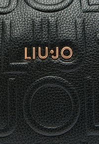 Sac à main en cuir noir texturé avec des motifs circulaires embossés, arborant un logo doré "LIU.JO" à l'avant.