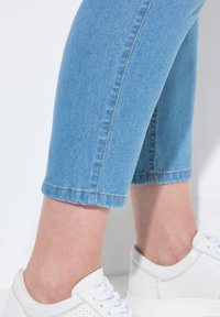 Světle modré džíny s krátkým střihem a přiléhavým designem, s běžným prošíváním. Spárovány s bílými teniskami s perforovanými detaily.