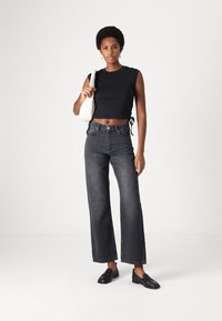 Black crop top with short sleeves, high-waisted dark gray wide-leg jeans, and black loafers; carrying a light-colored bag.