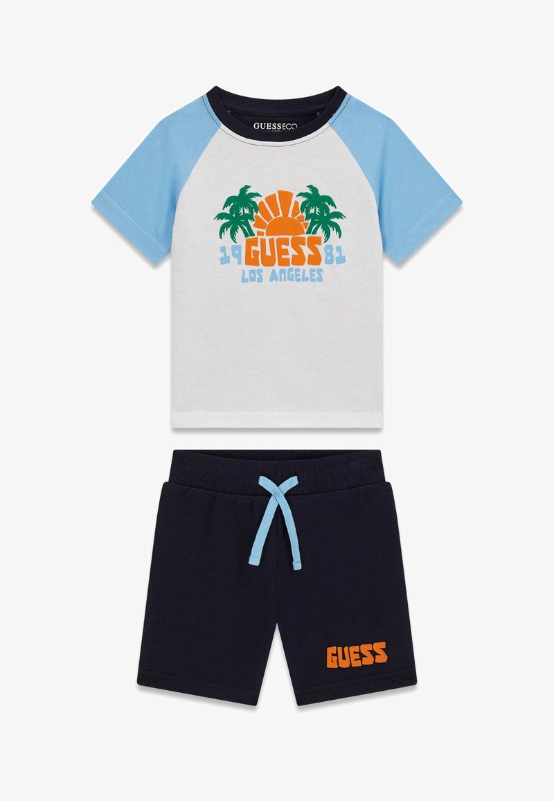 Short-sleeve kids' outfit with blue and white top featuring palm tree and sun graphic, navy shorts with blue drawstring and orange "GUESS" text.