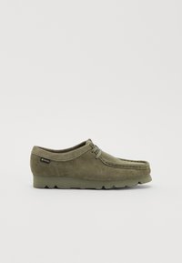 Chaussures en daim vert olive avec un bout rond, des détails en dentelle et une semelle en caoutchouc texturée. Présente un petit logo sur le côté.