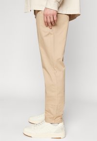 Chino en coton beige avec une coupe droite, dotés de poches latérales et d'une texture lisse. Associé à des baskets blanches avec des détails perforés.