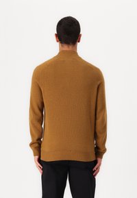 Maglione in maglia marrone con colletto alto, polsini e orlo a coste. La texture è morbida, con un design aderente e dettagli delle spalle senza cuciture.