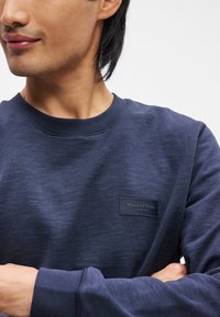 Sweatshirt azul marinho feito de tecido texturizado, apresentando um pescoço redondo e um rótulo retangular preto com "Marc O'Polo" em texto branco.