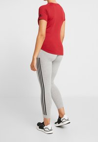 Maglietta atletica rossa a maniche corte con design testurizzato e logo nero sulla manica, abbinata a leggings grigi con strisce nere laterali.