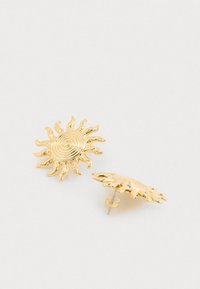 Zlate uhane v obliki sonca z vrtinčastim središčem in žarki, ki izžarevajo, z polirano kovinsko površino in zatičem na zadnji strani.