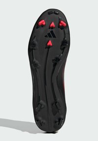 Semelle de crampons de football noire avec des picots triangulaires rouges. Présente des motifs texturés et un logo de marque visible. Forme arrondie avec un design clouté.