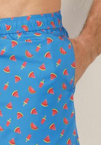 Pantalones cortos de baño azules con un patrón de sandías rosas y polos rojos, con una cintura elástica y una textura de tela suave.