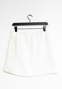 Bílá lněná sukně na černém ramínku, s jednoduchým áčkovým střihem, čistými okraji a hladkou texturou. Minimalistický design bez vzorů.