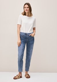 T-shirt léger blanc à manches courtes, jean en denim bleu taille haute, avec boutonnière à l'avant, poches, associé à des sandales tressées beige.