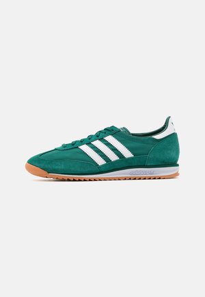 Zielony sneaker Adidas z białymi paskami, gumową podeszwą i zamszowymi detalami, widziany od zewnętrznej strony na białym tle.