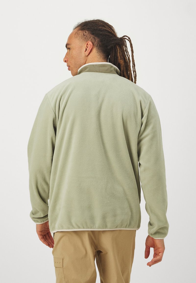 Lichtgroene fleece jack met hoge kraag, lange mouwen en elastische zoom. Zachte textuur met opvallende contrasterende stikdetails.