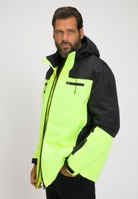 Hochsichtbare Jacke in Neon-Gelb und Schwarz, mit Kapuze, mit Reißverschlüssen versehenen Taschen und verstellbaren Bündchen. Strapazierfähiger Stoff mit glatter Textur.