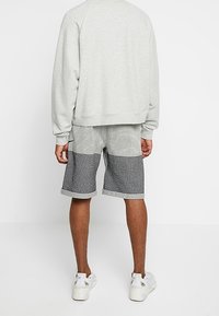 Ljusgrå fleece-tröja med en löst sittande passform, tillsammans med mönstrade grå shorts som har rutiga och enfärgade sektioner. Vita sneakers.