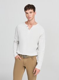 Maglietta Henley a maniche lunghe grigio chiaro con tre bottoni, abbinata a pantaloni beige. La maglietta presenta un tessuto strutturato e una vestibilità rilassata.