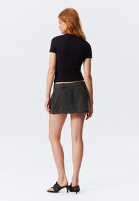 Aansluitend zwart t-shirt met korte mouwen, gecombineerd met een grijze denim mini-rok. De rok heeft een tailleband en een eenvoudig, strak ontwerp.