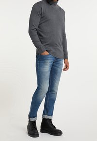 Maglione grigio a collo alto con maniche lunghe, abbinato a jeans slim fit azzurri sbiaditi e stivaletti neri con lacci, con risvolti ai polsini.