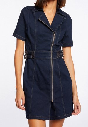 Frau trägt ein dunkelblaues Jeanskleid mit kurzen Ärmeln, Frontreißverschluss, Kragen und seitlichen Schnallendetails in der Taille.