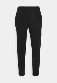 Černé tepláky mají stahovací pas, zúžené nohavice, boční kapsy a diskrétní detail loga na levé straně. Hladká textura.