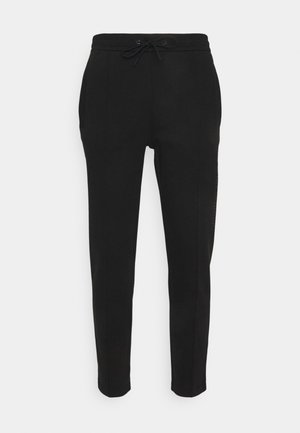 I pantaloni sportivi neri presentano una vita con cordino, gambe affusolate, tasche laterali e un discreto dettaglio con logo sul lato sinistro. Texture liscia.