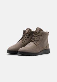 Botas de tobillo de ante marrón con un acabado texturizado, suela plana de goma negra y cordones a juego; presenta ojales reforzados y un parche con el logo.