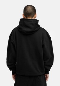 Schwarzer oversized Hoodie mit hohem Kragen und großer Tasche auf der Rückseite. Aus weichem Stoff gefertigt, mit überschnittenen Schultern und langen Ärmeln.