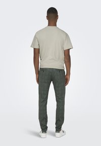 Lichtgrijze katoenen t-shirt en donkergroene geruite broek. Witte sneakers met groene accenten. Uitzicht van achter.