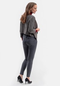 Grijze cropped jas met een vloeibaar ontwerp, gecombineerd met donkere denim skinny jeans en zwarte hoge hakken. Glad textuur, getailleerde pasvorm.