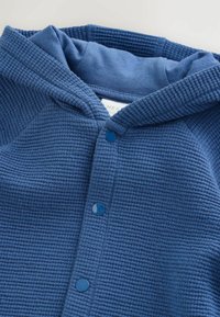 Blue waffle-knit baby cardigan with hood and three snap buttons, laid flat on a white surface.