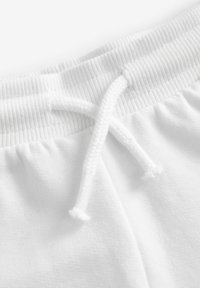 Pantalons de jogging blancs en coton avec un cordon de serrage. La taille présente une texture côtelée, et le tissu semble doux et lisse.