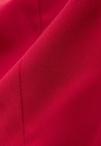 Primer plano de tela roja vibrante que muestra una textura detallada de tejido diagonal y una línea de costura que atraviesa el área central.