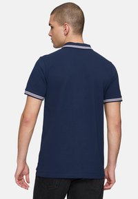 Donkerblauwe poloshirt met korte mouwen, voorzien van een gestreepte kraag en mouwranden. Gemaakt van soepele katoen met een klassieke pasvorm.
