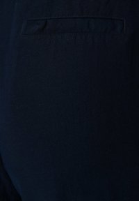 Tissu bleu marine foncé avec une texture lisse, comportant une petite poche passepoilée rectangulaire à l'arrière. Design simple et discret.