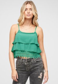 Zeleni, slojeviti crop top s čipkastim rubom. Izrađen od lagane tkanine, sa tankim podesivim trakama. Nosite s tamnim, istrošenim trapericama.