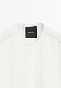 White blouse with lace trim on shoulders and a round neckline with a small stand-up collar, labeled Massimo Dutti.