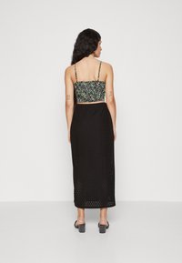 Svart, lang skjørt med perforert tekstur, parret med en kort, blomstermønstret topp med spagettistropper og smock-detaljer.