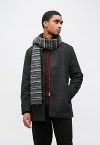 Casaco de lã cinza escuro com gola alta, apresenta fecho com botões e bolsos laterais. Combinado com um cachecol riscado cinza e preto.