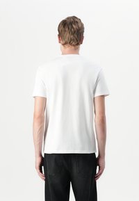 Vit kortärmad t-shirt med rund hals, gjord av bomull, med en slät textur. Bärs tillsammans med svarta denimjeans som har bakfickor.