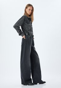 Svart denimjacka med två bröstfickor och knappar, i kombination med överdimensionerade svarta jeans. Båda plaggen har en urtvättad textur och en vida passform.