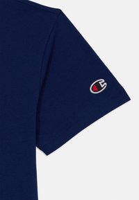 T-shirt azul marinho com mangas curtas. Apresenta um pequeno logótipo bordado em vermelho e branco na manga. Textura de algodão suave.