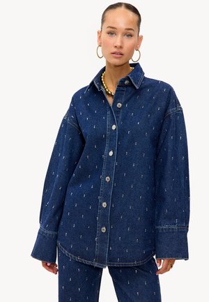 Chemise en denim bleu foncé avec un devant à boutons. Dotée d'un col, de manches oversized et d'accents métalliques dans un motif éparpillé.