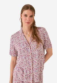 Camicia a maniche corte con bottone, caratterizzata da un motivo floreale rosa e viola su uno sfondo crema, dotata di tasca e vestibilità comoda.