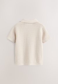 Strikket kortærmet polo i off-white med et tekstureret mønster og en krave. Jævnt fordelte vandrette linjer over det hele.