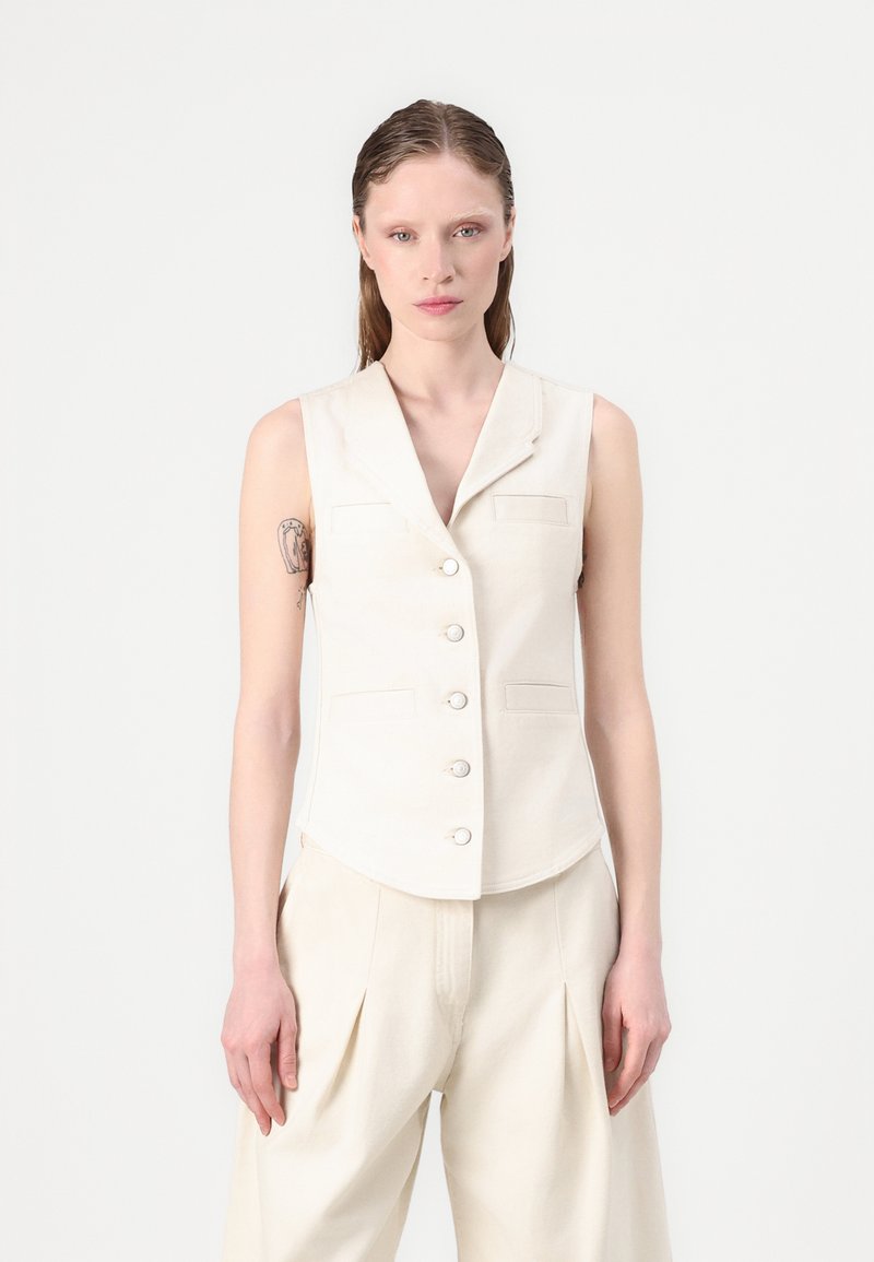 Crème mouwloos vest met een geknipt kraag, vijf knopen en twee voorkwabben. Textuurstof; gecombineerd met bijpassende lichtgekleurde broek.