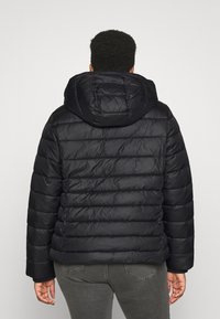 Černá péřová bunda s kapucí, s horizontálně prošívaným designem, texturovanou tkaninou a pružnými manžetami. Pohled z zad ukazuje volný střih.